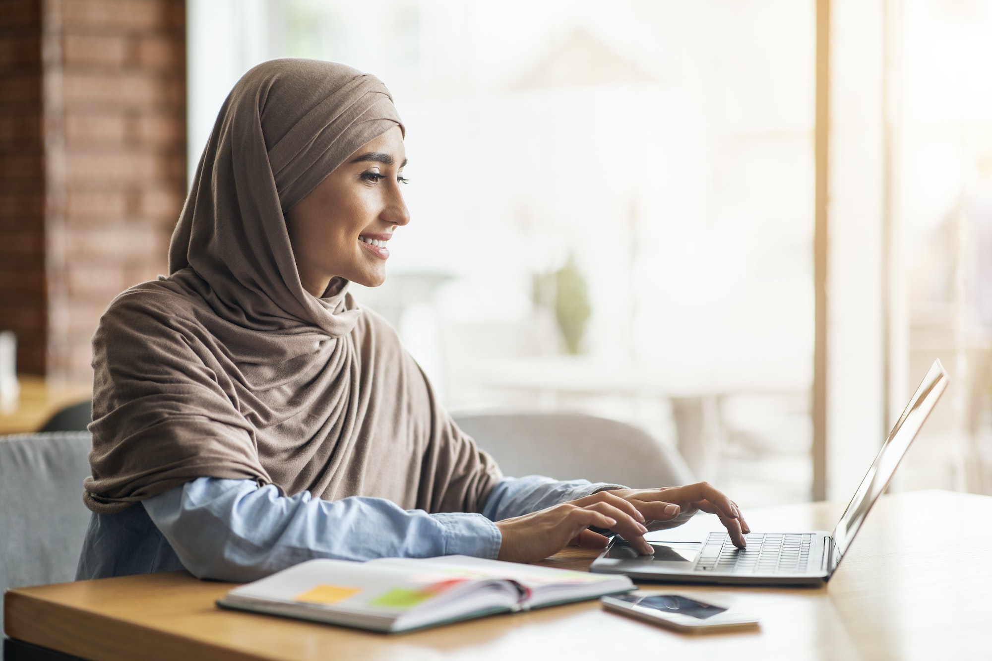Cheerful girl in hijab sitting at cafe, looking for job Cheerful girl in hijab sitting at cafe, looking for job