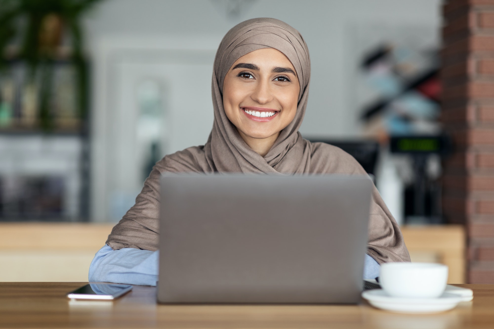 Cheerful muslim woman in hijab working online at cafe