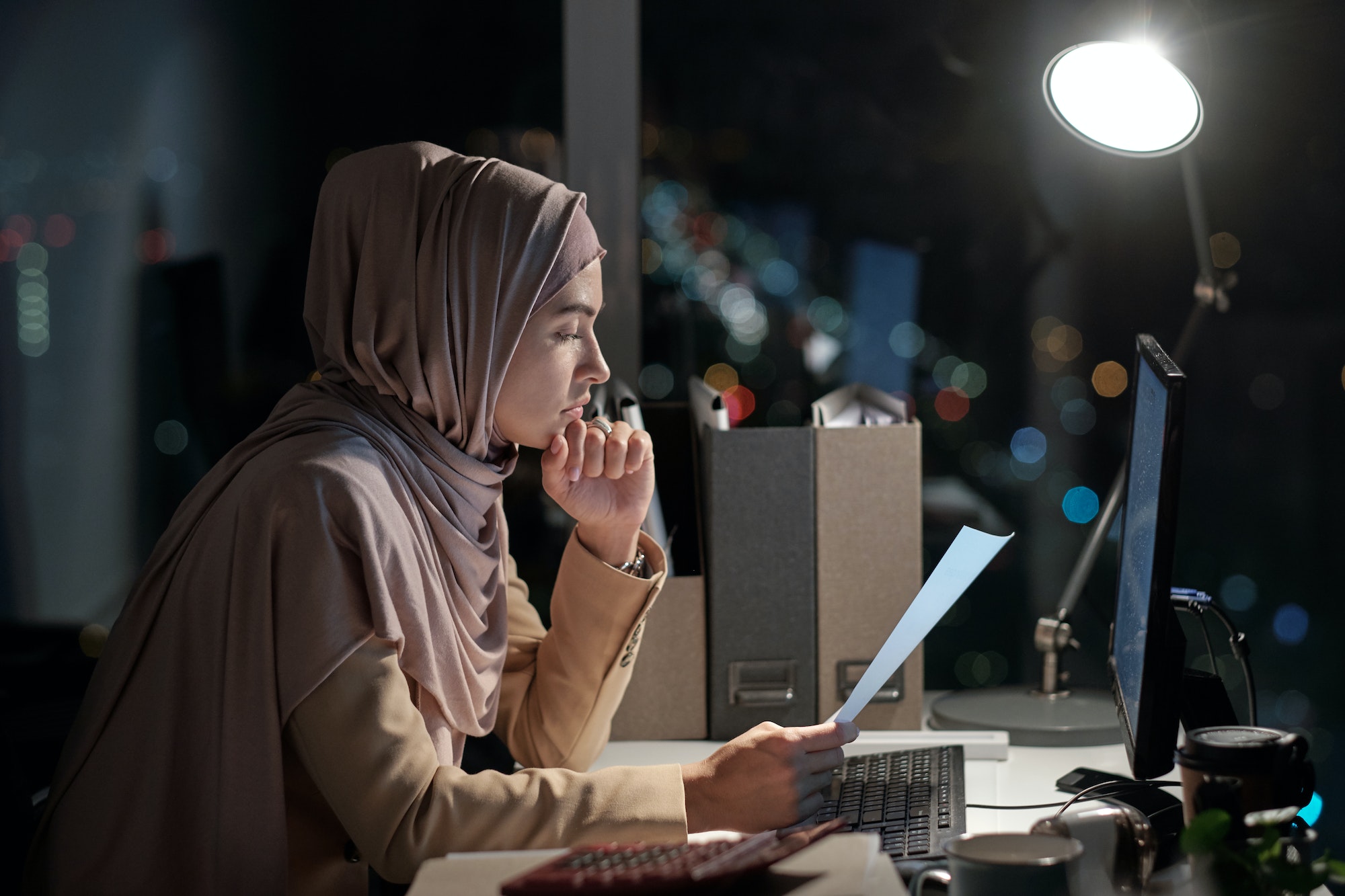 Side view of young businesswoman in hijab looking through papers